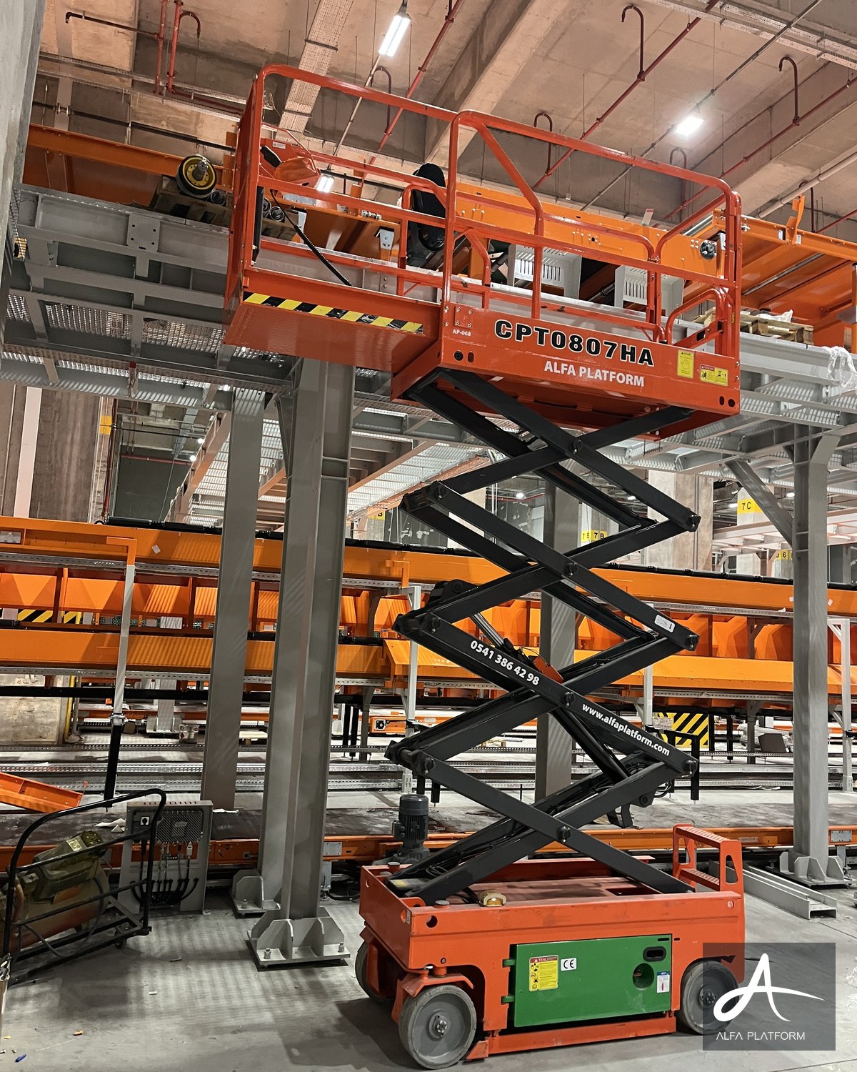Depo benzeri bir iç mekanda, makaslı platform yukarı kalkmış.