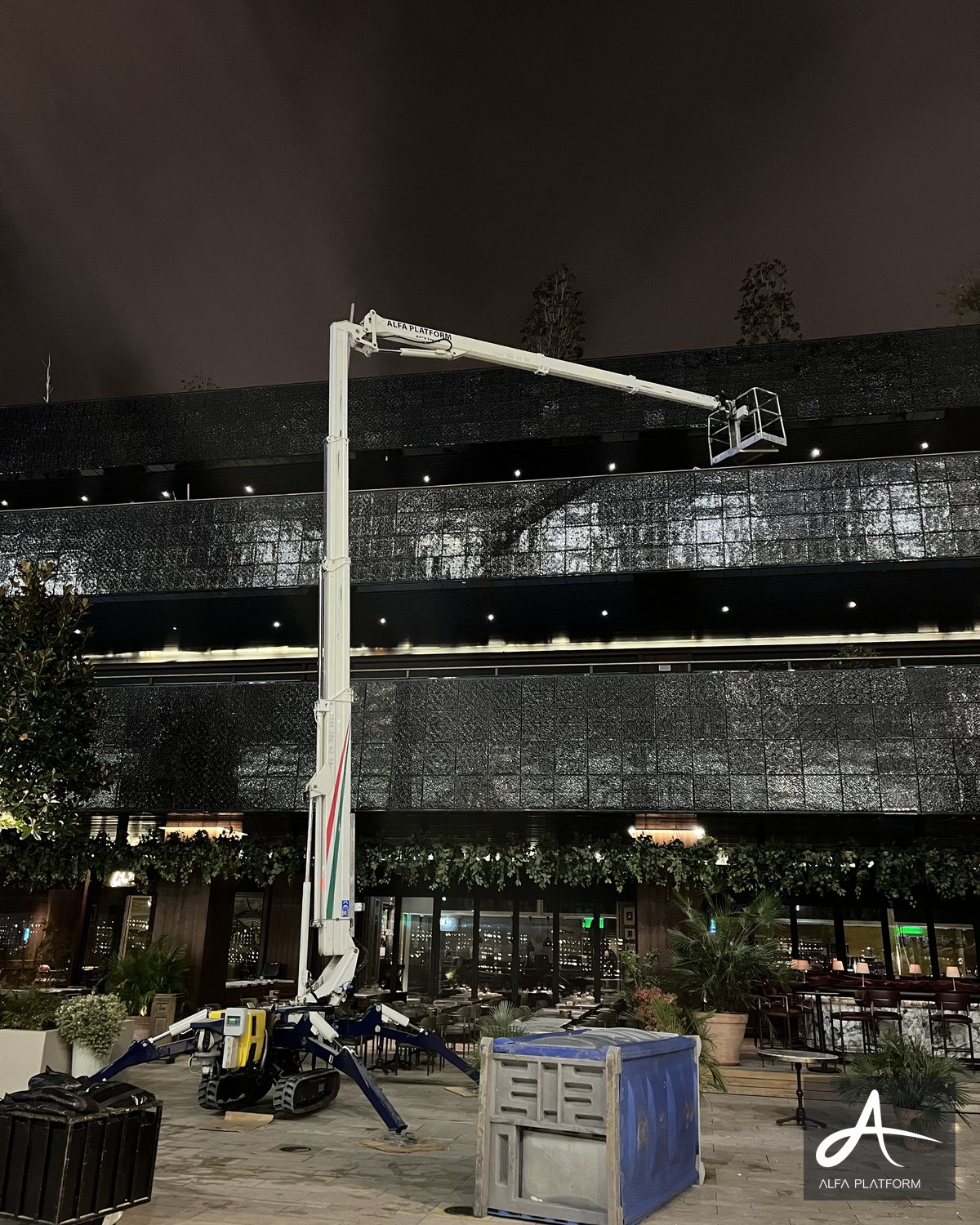 Bir örümcek platform, gece vakti bir binanın dış cephesinde çalışıyor.